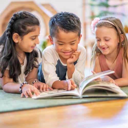 Three children look through the pages of a book