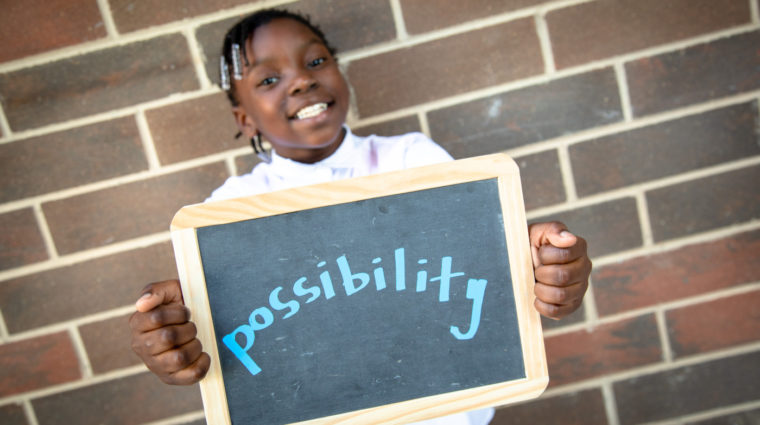 Girl holding chalk board sign that reads 'possibility'